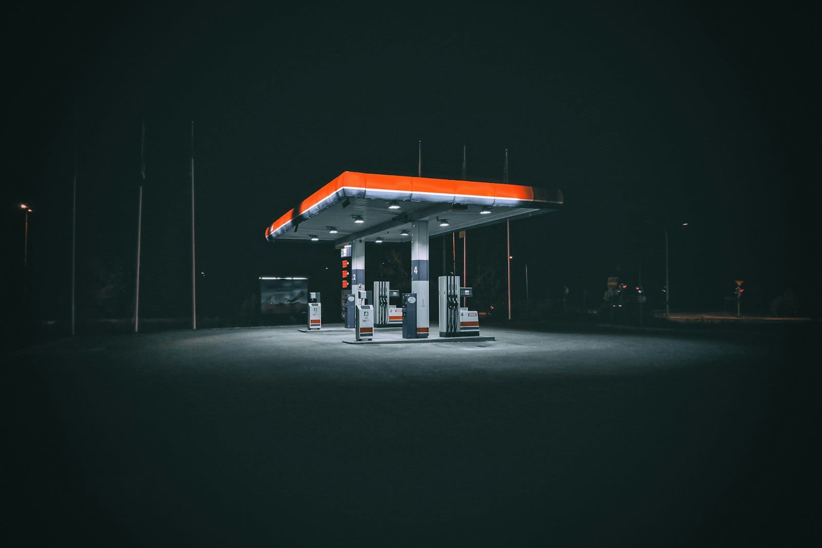 A deserted fuel station forecourt at night, canopy lit, no vehicles present.